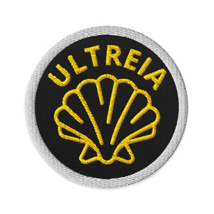 May include: A circular embroidered patch featuring a black background with a yellow scallop shell icon centred in the middle. The word ULTREIA is stitched in yellow capital letters in an arc above the shell. The patch has a white stitched border.