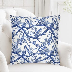 May include: A square throw pillow featuring a white background with a repeating blue pattern of birds perched on flowering branches. The design includes detailed illustrations of various birds, blossoms, and small butterflies across the fabric.
