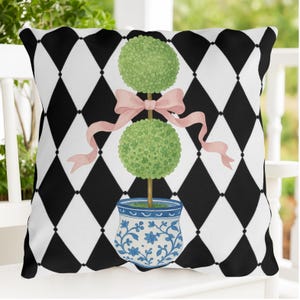 Peut inclure: Coussin décoratif avec un motif de losanges noirs et blancs. Il présente une illustration à l'aquarelle d'un arbre topiaire avec un nœud rose, dans un pot floral bleu et blanc.
