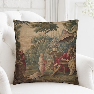 May include: A square throw pillow featuring a detailed tapestry-style print of an outdoor scene with figures in historical attire, lush trees, a large umbrella, and stone structures in muted earth tones of brown, green, and deep red.