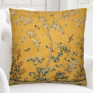 May include: A square throw cushion featuring a mustard yellow background with a printed pattern of thin brown tree branches, white blossoms, green leaves, and various birds in flight and perched on the branches throughout the design.