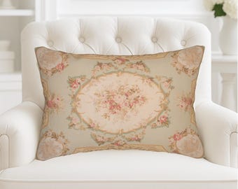 May include: Rectangular decorative pillow with a floral pattern. The pillow features a central oval design with pink roses and green accents on a light green background. The pillow is placed on a white armchair.