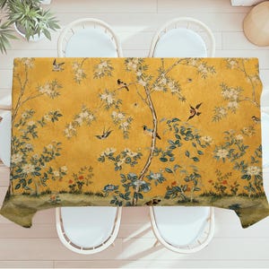May include: A rectangular tablecloth featuring a mustard yellow background with a printed pattern of thin brown tree branches, white blossoms, green leaves, and various small birds in flight and perched on the branches across the fabric surface.
