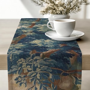 Könnte beinhalten: Blau-beiger Tischläufer mit einem Waldmotiv. Der Läufer zeigt Bäume und Blätter in Blau-, Grün- und Brauntönen. Eine weiße Tasse und Untertasse befinden sich auf dem Läufer, im Hintergrund eine Vase mit Blumen.