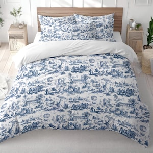 May include: A bed with a white duvet and pillowcases. The duvet cover and pillowcases feature a blue and white toile pattern depicting scenes of people, hot air balloons, and landscapes. The bed is set against a wooden headboard.