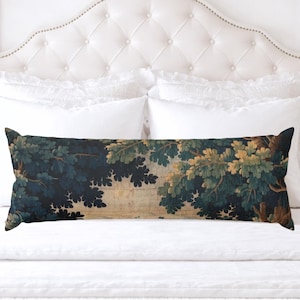 May include: A long, rectangular decorative pillow with a tapestry design featuring a forest scene in shades of blue, green, and tan. The pillow is placed on a white bed with a tufted headboard and white bedding.