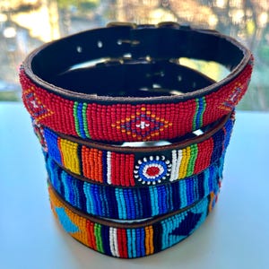 Peut inclure: Quatre colliers de chien en perles colorées empilés les uns sur les autres. Les colliers sont en cuir et présentent une variété de couleurs vives, notamment le rouge, le jaune, le bleu et le vert.