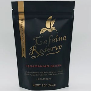 May include: A black bag with gold lettering that reads "Whole Bean Coffee", "Cafeina Reserve", "Panamanian Geisha", "Light Body, Honey, Citrus & Floral Flavors. Fruit Notes of Peach, Papaya, Berry, Lemon. Floral Notes of Jasmine", "Medium Roast", and "Net Wt. 8 oz. (226 g)".