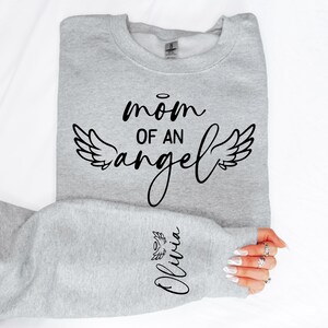 May include: Grey sweatshirt with the text "mom of an angel" and a pair of angel wings. The text "Olivia" is written on the sleeve with a small angel wing.