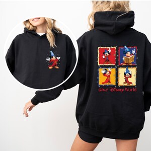 May include: Black hooded sweatshirt with a colourful graphic of Mickey Mouse as a sorcerer on the back. The graphic features four different poses of Mickey Mouse in a square frame with the text "Walt Disney World" below.