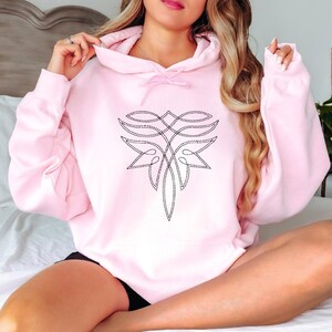 Puede incluir: Una sudadera con capucha rosa claro con un dise&ntilde;o floral negro estilizado en la parte delantera. El dise&ntilde;o est&aacute; hecho de l&iacute;neas discontinuas. La sudadera con capucha tiene una capucha con cord&oacute;n y mangas largas. El modelo lleva un pantal&oacute;n corto negro.