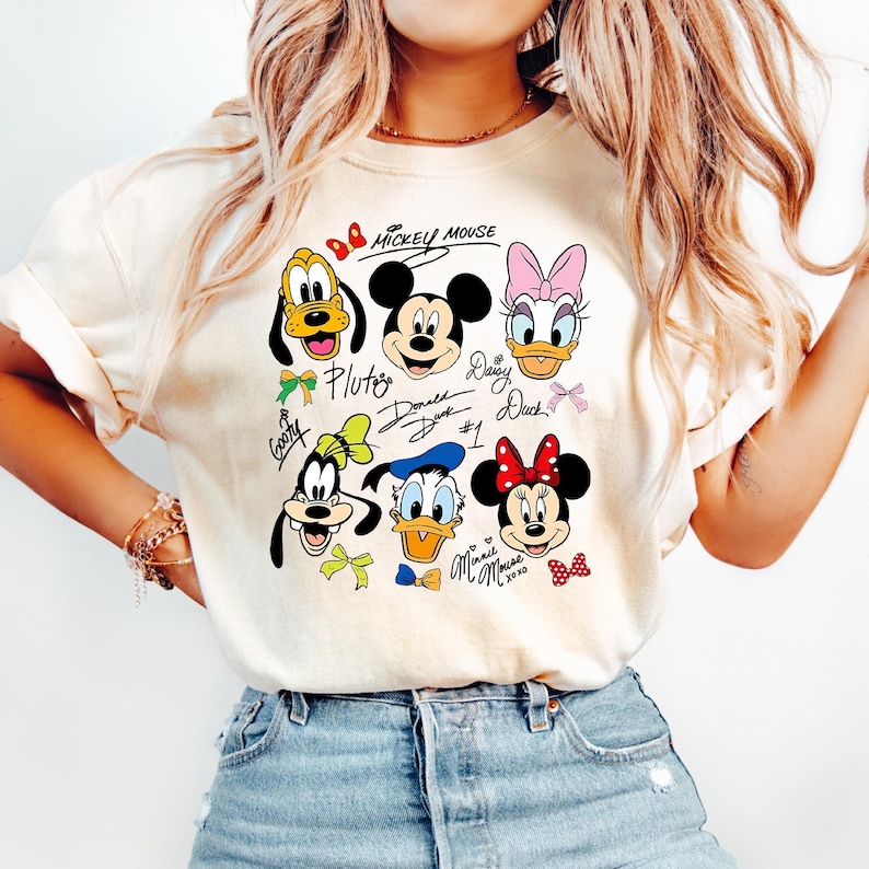 Peut inclure: T-shirt cr&egrave;me avec des personnages Disney : Mickey Mouse, Pluto, Donald Duck, Daisy Duck, Minnie Mouse et Dingo. Le texte "Mickey Mouse" est en haut, avec les noms des personnages en dessous de chaque image.