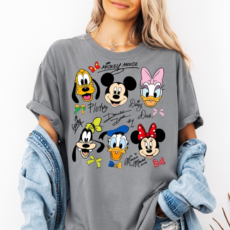 Peut inclure: T-shirt gris avec un motif color&eacute; de Mickey Mouse et ses amis, dont Pluto, Dingo, Donald Duck, Daisy Duck et Minnie Mouse. Le motif comprend les noms et les signatures des personnages. Les manches du t-shirt sont retrouss&eacute;es.