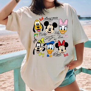 Peut inclure: T-shirt cr&egrave;me avec un graphisme color&eacute; de Mickey Mouse et ses amis, dont Pluto, Dingo, Donald Duck, Daisy Duck et Minnie Mouse. Le texte "Mickey Mouse" est au-dessus des personnages. Le t-shirt est de coupe ample.