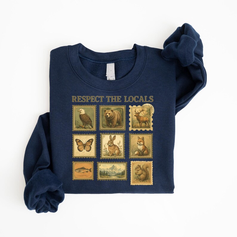 May include: Navy blue sweatshirt with the text "RESPECT THE LOCALS" above a grid of vintage-style postage stamps featuring various animals, including an eagle, bear, deer, butterfly, rabbit, fox, fish, and squirrel.