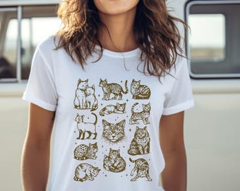 May include: White t-shirt featuring a collection of illustrated cats in various poses and patterns. The cats are depicted in a sepia tone, creating a vintage aesthetic. The shirt is a classic crew neck style.