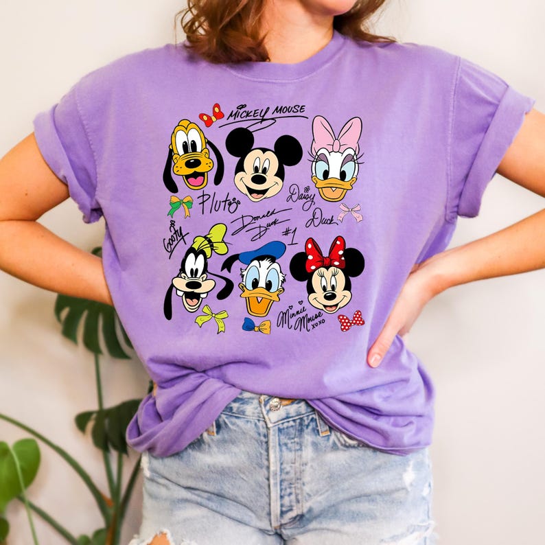 Peut inclure: Un t-shirt lilas avec un motif de Mickey Mouse et ses amis. Le motif comprend Pluto, Mickey, Daisy Duck, Dingo, Donald Duck et Minnie Mouse, avec leurs noms et signatures. Le t-shirt a des manches retrouss&eacute;es.