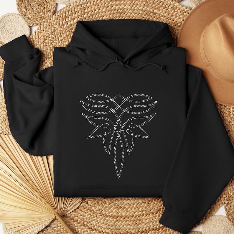 Puede incluir: Sudadera con capucha negra con un dise&ntilde;o bordado blanco en la parte delantera. El dise&ntilde;o es un patr&oacute;n abstracto y sim&eacute;trico con apariencia cosida. La sudadera tiene capucha y mangas largas, y est&aacute; doblada sobre una superficie tejida.