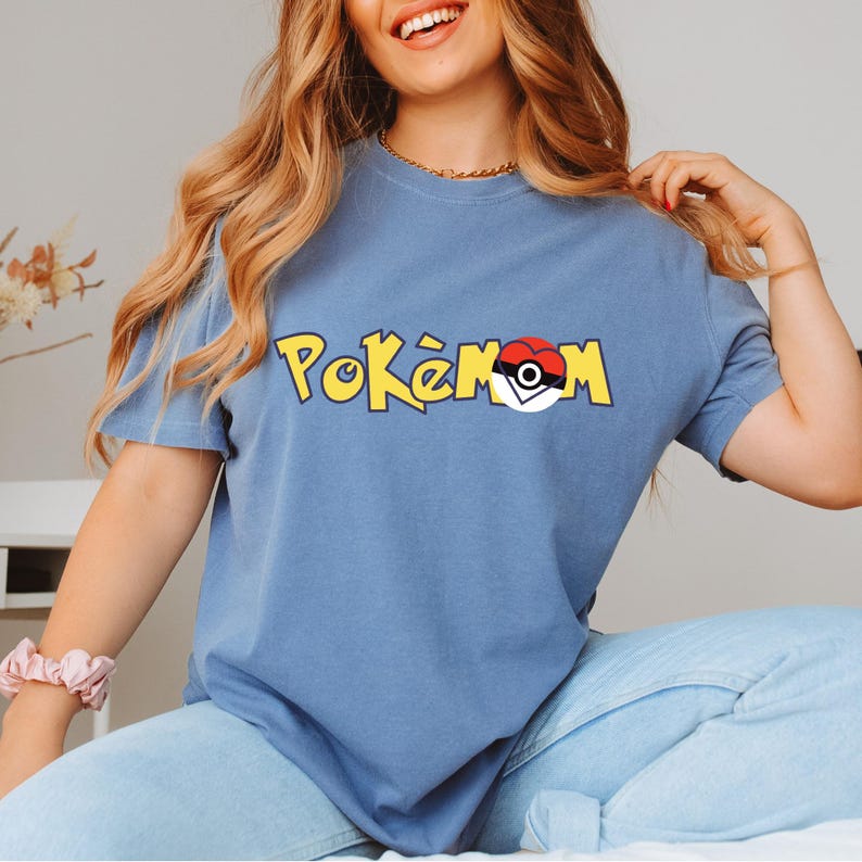 Puede incluir: Una camiseta azul con la palabra "Pok&eacute;mon" en letras amarillas y un dise&ntilde;o de Pok&eacute; Ball rojo y blanco. La camiseta de manga corta est&aacute; hecha de un material suave.