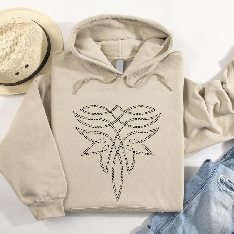 Puede incluir: Sudadera con capucha beige con un dise&ntilde;o floral abstracto negro cosido en la parte delantera. La sudadera tiene una capucha con cord&oacute;n y un bolsillo de canguro. Se ven un sombrero beige y una chaqueta vaquera.