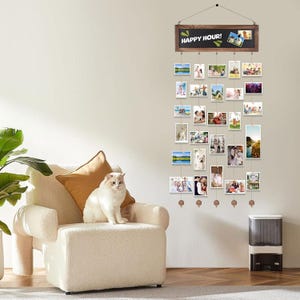 Peut inclure: Un présentoir photo mural avec un cadre en bois et un tableau noir avec l'inscription "HAPPY HOUR!". L'affichage contient plusieurs petites photos suspendues par des cordes. Un chat blanc est assis sur un fauteuil crème.