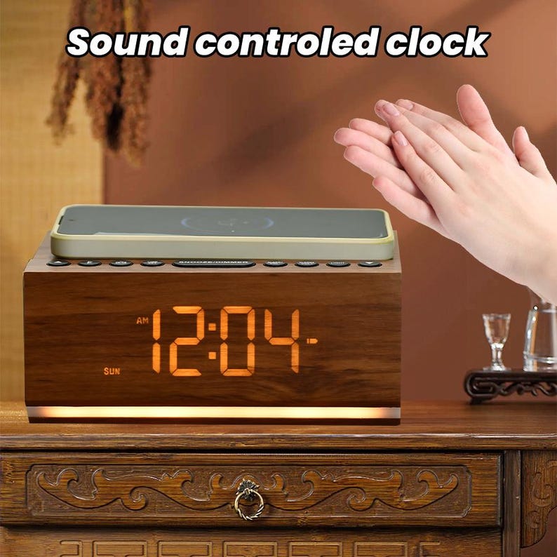 May include: A wooden alarm clock with a digital display showing the time 12:04 AM. The clock has a built-in wireless charging pad for a smartphone. The clock is on a wooden table with a carved design. The text "Sound controlled clock" is displayed above the clock.