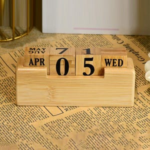 May include: A wooden desktop calendar with a light brown finish. The calendar features a date display with the month, day, and day of the week. The date is set to April 05, Wednesday.