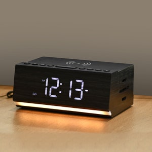 May include: Black wooden alarm clock with a white digital display showing 12:13 AM. The clock has a built-in wireless charging pad and a white light underneath.