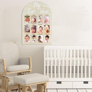 May include: A wooden plaque with a light beige finish, arched at the top, featuring the words 'My First Year' in a handwritten style. It has twelve photo frames labeled with the numbers one through twelve, each containing a baby photo. The plaque is designed for displaying monthly baby pictures.