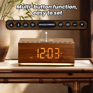 May include: A wooden alarm clock with a digital display showing 12:03 AM. The clock has a built-in wireless charging pad and multiple buttons for setting the time, alarm, and other functions. The clock is sitting on a wooden table.