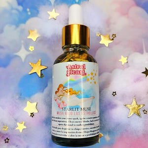 May include: A glass bottle of essential oil with a gold lid and label. The label says "Astral Heart" and "Starlit Muse Musa Bajo Las Estrellas". The bottle is sitting on a pink and blue background with gold stars.