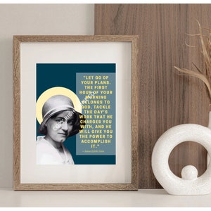 Puede incluir: Impresión enmarcada con un retrato en blanco y negro de una mujer y una cita en un recuadro color turquesa. La cita dice: "Deja ir tus planes. La primera hora de tu mañana pertenece a Dios..." Un jarrón blanco con plantas secas está a la derecha.