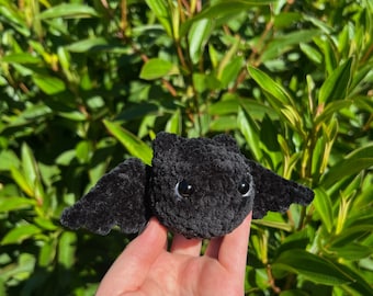 May include: A black crocheted bat with white eyes. The bat is being held in a hand.