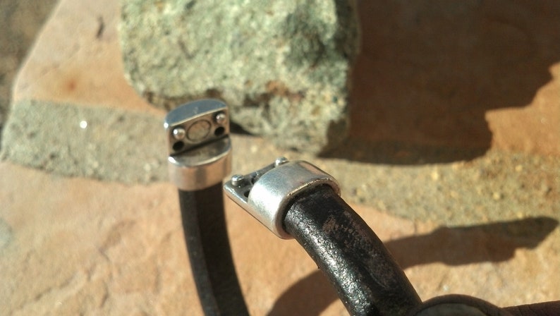 May include: A black leather bracelet with silver magnetic clasps. The bracelet is made from thick, durable leather and has a simple, elegant design.