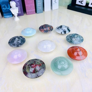 May include: Ten different coloured and patterned coasters in the shape of a flying saucer. The coasters are made of stone and have a variety of colours and patterns, including red, green, blue, white, and black.