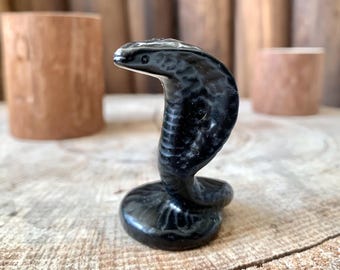 May include: Black obsidian cobra figurine with a smooth, polished finish. The figurine is in a coiled position with its head raised.