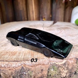 以下が含まれることがあります： 黒くてスタイリッシュで未来的なデザインの玩具の車。車は低く、シャープで角度のあるデザインです。車は木製の表面の上に置かれています。