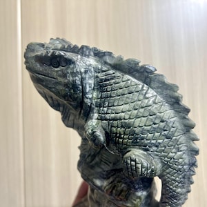 May include: A detailed sculpture of a lizard, carved from a stone with shades of grey and green. The lizard is posed in a dynamic position, with intricate scale and texture details. The sculpture is a decorative item.