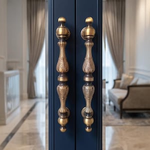 May include: Close-up of two ornate, antique-style door handles. The handles are made of a gold-colored metal with intricate floral and scrollwork designs. They are mounted on a dark blue door, creating a striking contrast.