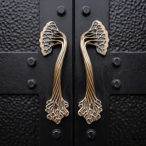 May include: Close-up of a pair of black doors with ornate brass handles. The handles are shaped like stylized trees, with intricate branch and leaf details. The doors have a textured surface and are secured with black bolts.