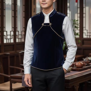 Könnte beinhalten: Eine marineblaue Samtweste mit goldenen Zierleisten und Knöpfen. Die Weste wird über einem weißen Hemd mit Kragen getragen. Die Weste hat einen Stehkragen und einen einzigartigen Verschluss. Das Outfit wird mit einer schwarzen Hose abgerundet.