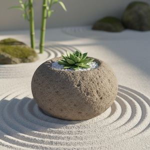 Könnte beinhalten: Ein runder, strukturierter Steintopf mit einer Sukkulente und weißen Kieselsteinen. Der Topf steht auf einem Sandbett mit geharkten Mustern, mit Bambusstängeln und moosigen Felsen im Hintergrund. Die Sukkulente hat grüne Blätter.