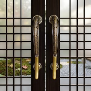 May include: Close-up of a pair of dark brown wooden doors with ornate brass handles. The handles have a curved design with a wood grain pattern and are mounted on circular bases. The background shows a grid-patterned window with a view of a garden.