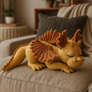 Puede incluir: Un dragón tejido a ganchillo en tonos amarillos y marrones, descansando en un sofá. El dragón tiene alas detalladas, una larga cola y los ojos cerrados, lo que le da una apariencia tranquila. Este juguete de peluche hecho a mano es un artículo decorativo caprichoso.