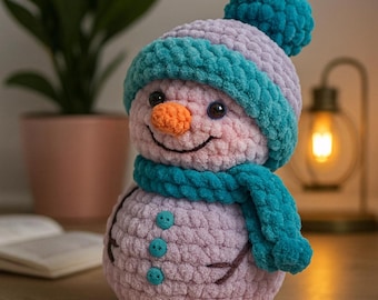 May include: A handmade snowman plushie with a pink body, a lavender hat, and a teal scarf. The snowman has a carrot nose, button eyes, and a stitched smile. The hat has a teal brim and a teal pom-pom.