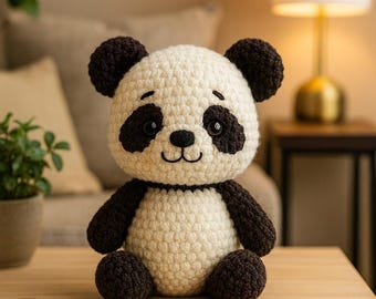 May include: A handmade crochet panda bear with a cream-colored body and black accents on the ears, eyes, arms, and legs. The panda has a smiling face and is sitting upright. This soft toy is perfect for a child's room or as a decorative item.