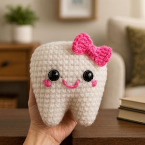 Peut inclure: Une dent crochetée avec un nœud rose, des yeux en boutons noirs et une bouche rose souriante. Le jouet en peluche fait à la main est blanc et a des joues roses. La dent est un design mignon et fantaisiste.