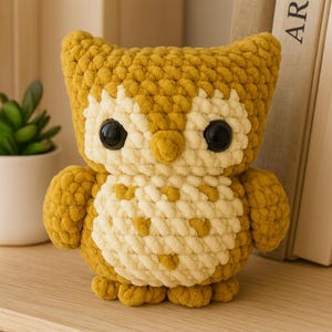 May include: A handmade, plush owl toy in shades of yellow and cream. The owl has large, black button eyes and a cream-colored chest with yellow heart-shaped accents. The soft, textured yarn gives the owl a cuddly appearance. A decorative item.