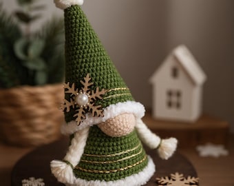 May include: A handmade Christmas gnome with a green crocheted hat and body, adorned with a wooden snowflake and gold trim. The gnome has a white beard and a fluffy white pom-pom on top of the hat. A festive holiday decoration.