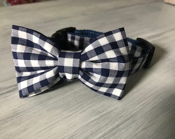 Może przedstawiać: Muszka w kratę gingham w kolorze granatowym i białym, przymocowana do czarno-granatowego kołnierza dla psa w kratę gingham.